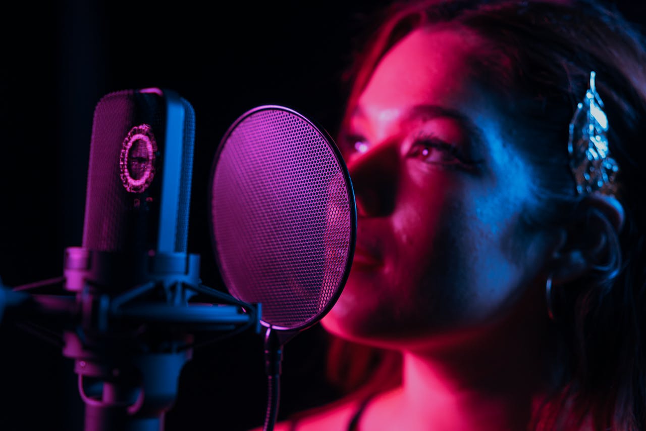 Close-up of a woman singing into a microphone in a dimly lit recording studio.